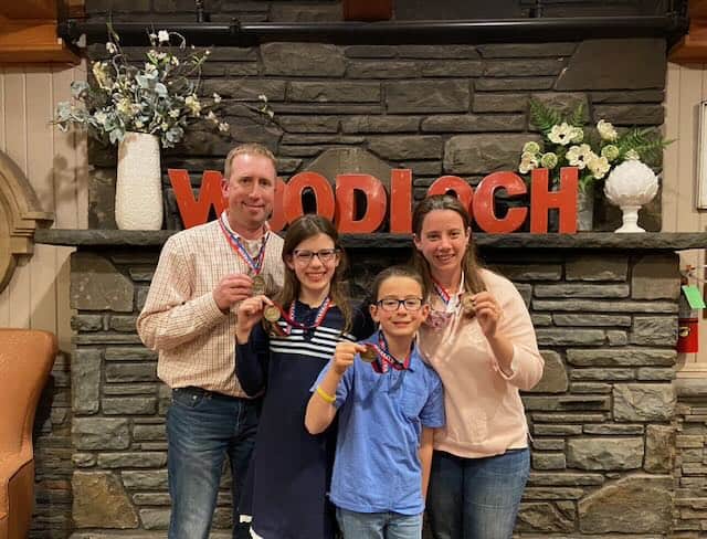 family posing in front of Woodloch resort sign holding medals